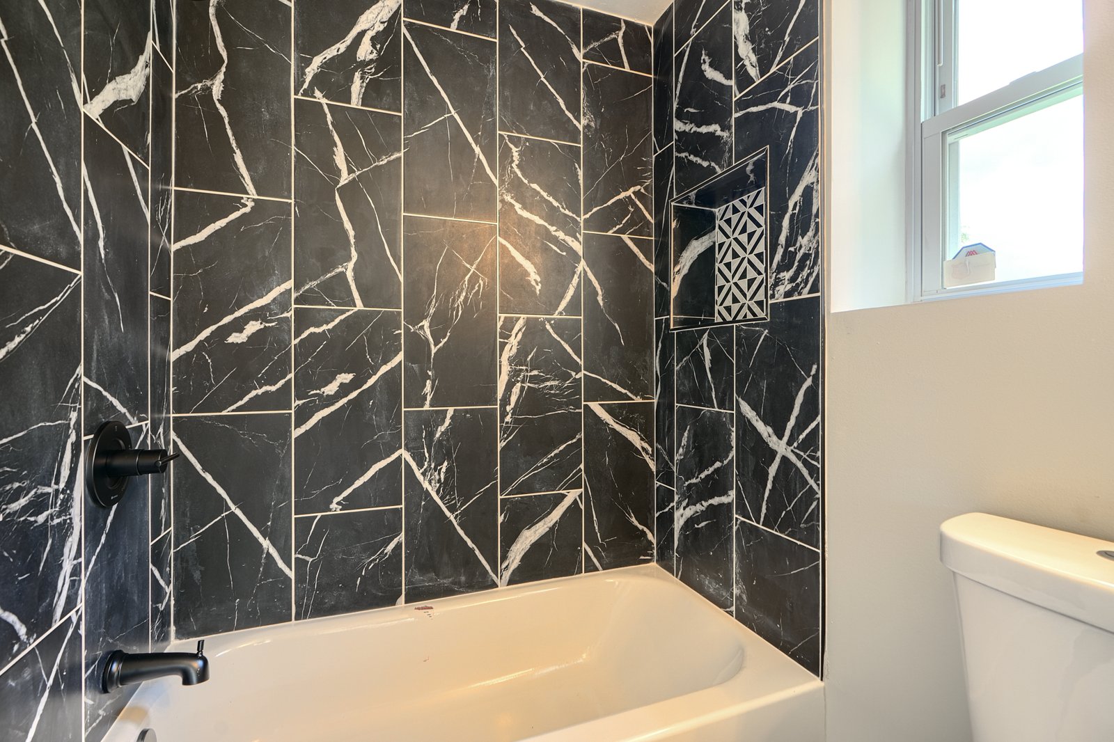 Bathroom with black marble tile surround and decorative niche