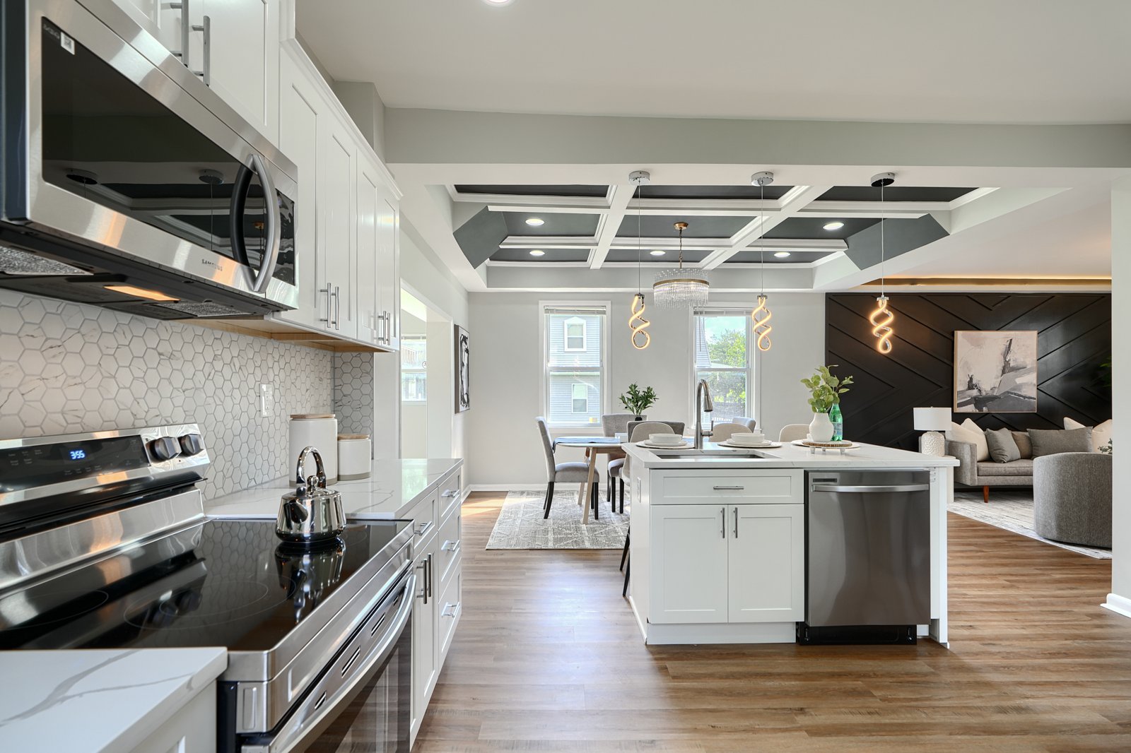 Full kitchen showing white cabinetry, hex backsplash, coffered ceiling, and living area